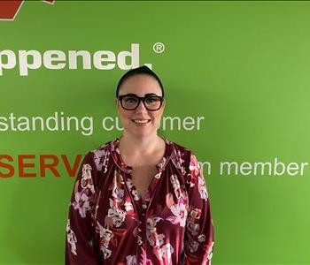 Sarah Raymond standing in front of a green wall with the SERVPRO logo and mission statement below it.
